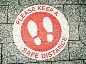 Close-up of a social distancing sign on pavement urging safe distance.