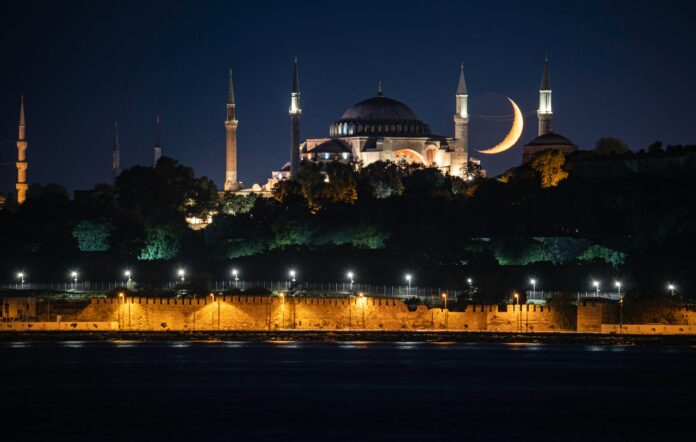 A stunning nighttime view of Hagia Sophia Grand Mosque in Istanbul with a crescent moon in the backdrop.