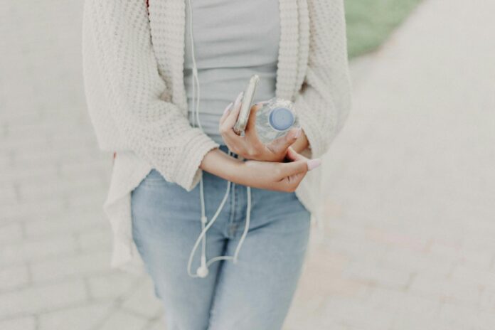 Casual young woman outdoors with water bottle and smartphone, enjoying a sunny day.