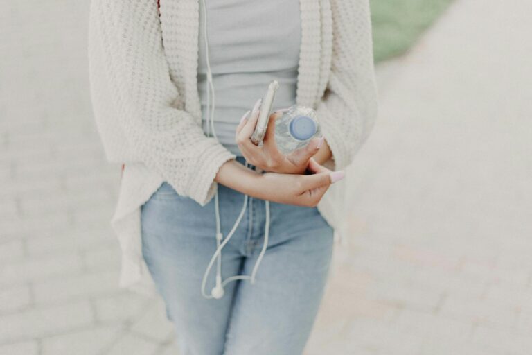 Casual young woman outdoors with water bottle and smartphone, enjoying a sunny day.